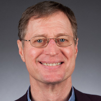 Professor Rob Horner, a man with light brown hair and blue eyes, wearing glasses and an open-necked blue shirt. The background is a neutral gradient of blue-grey.