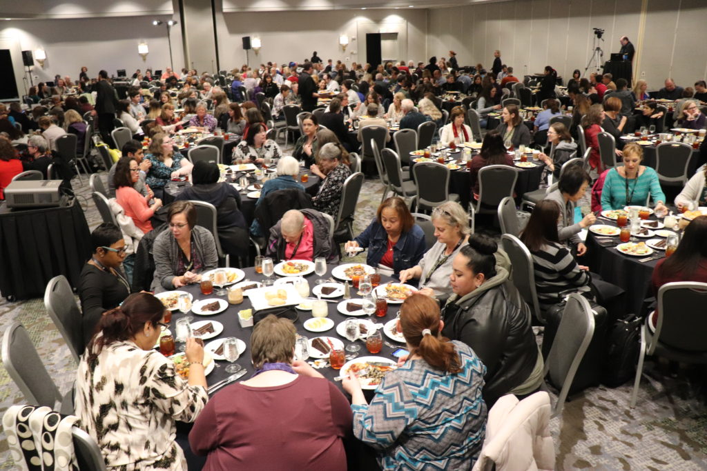 A photograph of the audience of the Membership Luncheon. A large banquet room of hundreds of people sitting at round tables.
