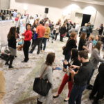 A wide-angle photograph of the poster reception: a room full of people mingling in groups around posters tacked up on rows of easels.