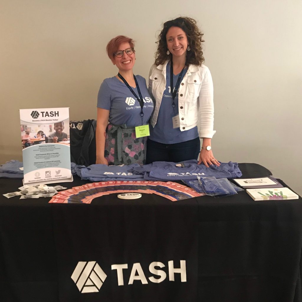 A photograph of the TASH membership table. Raquel Rosa and Ali DeYoung are standing behind it, both wearing blue TASH t-shirts.