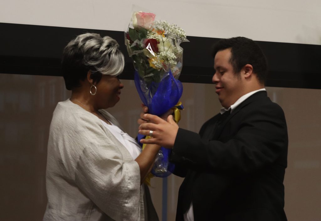 A photograph of a man in a suite handing Barbara Ransom a large bouquet of flowers.