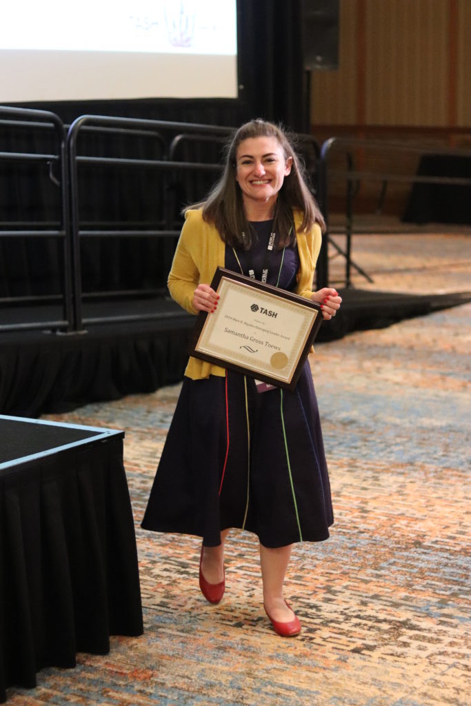 A photograph of Samantha Gross-Toews rounding the corner of the awards stage with her plaque in hand.