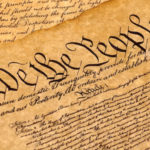 A detail of the U.S. Constitution, showing the opening line, We the People, in a complicated black cursive