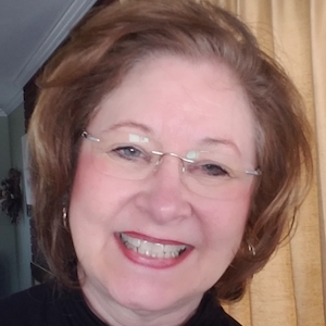 A photograph of Gail Fanjoy. She has auburn parted hair, low-peofile glasses and is wearing a black shirt.