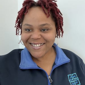 A portrait of Kyra Harvey. She has short black dreadlocks with red highlights. She is wearing a navy pullover with the SEEC emblem on the left front.